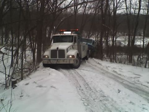 1992 Ford Bronco - A white tow truck pulls a blue car through a snowy, wooded area.