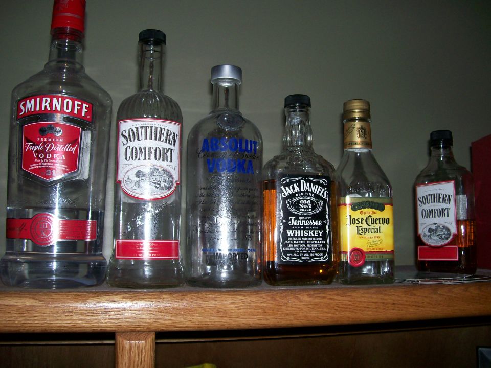 Several bottles of liquor including Smirnoff, Southern Comfort, Absolut, Jack Daniels, and Jose Cuervo on a shelf