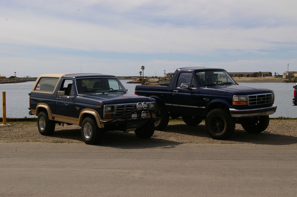 Blue Ford Bronco and a dark blue Ford pickup truck parked by the water