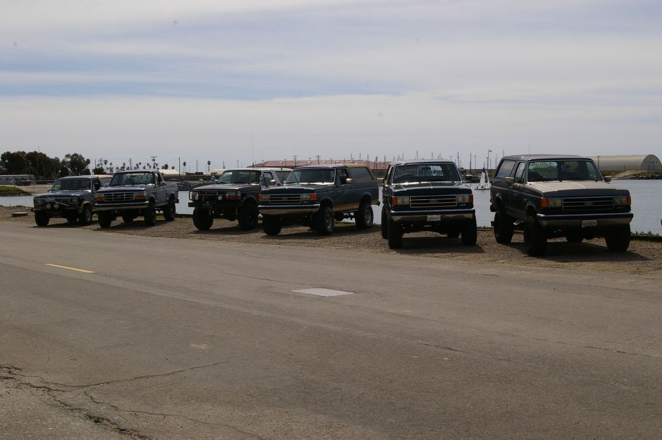 Several Ford Bronco SUVs and pickup trucks parked by the water