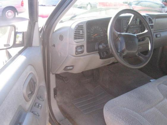 Driver's side interior of a GMC pickup with gray dash, steering wheel, and cloth bench seat