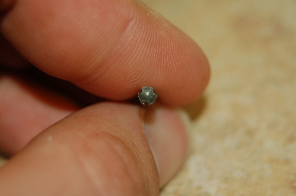 Close-up of a small, three-pronged metal fastener held between two fingers