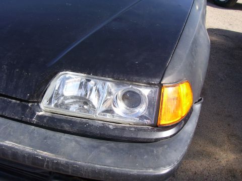1993 Mazda MX-6 - Close-up of the front corner of a black 1993 Mazda MX-6, showing the headlight and bumper detail.