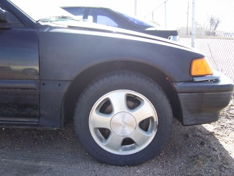 1993 Mazda MX-6 - Close-up view of a car's front wheel and fender, with another vehicle in the background.