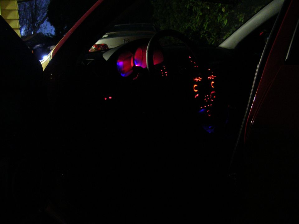 Night interior of a red Mazda 3 lit only by glowing gauges and climate control dials