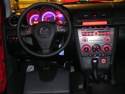 2007 Mazda 3 - The interior of a 2007 Mazda 3 shows a dashboard with illuminated gauges and a center console with red accents.