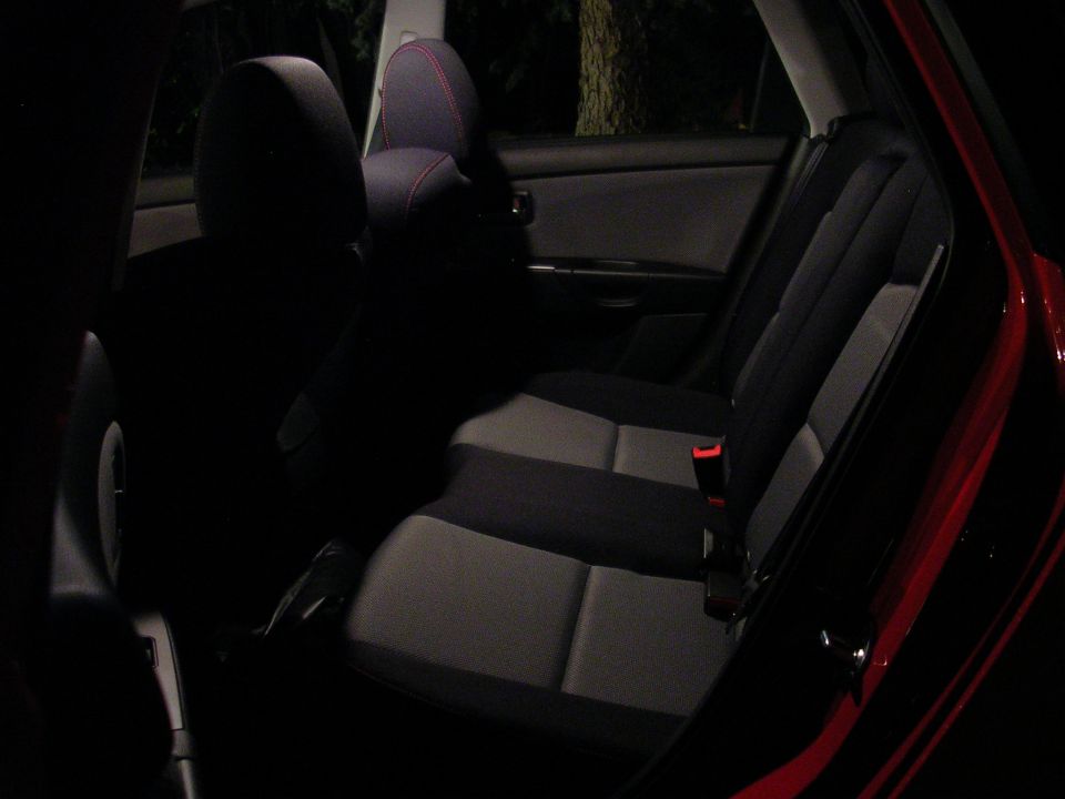 Rear bench seat of a red hatchback at night, gray and black cloth with red stitched headrest