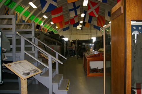 1986 Ford Bronco - Interior view of a museum nautical flags hanging from the ceiling and military vehicles displayed on the floor.