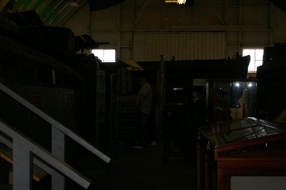 Interior of a museum or warehouse with exhibits and a person standing near stairs