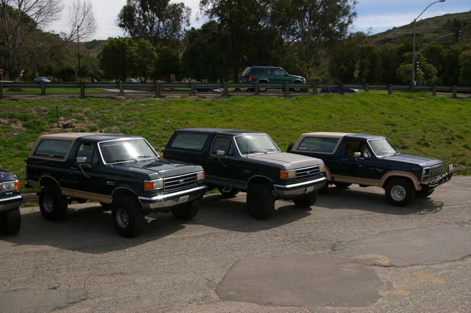 Three dark Ford Broncos parked side-by-side, one with a tan top