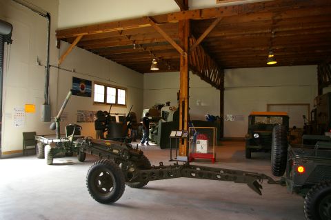 1986 Ford Bronco - Museum interior displaying military equipment including artillery, a truck, and a jeep.
