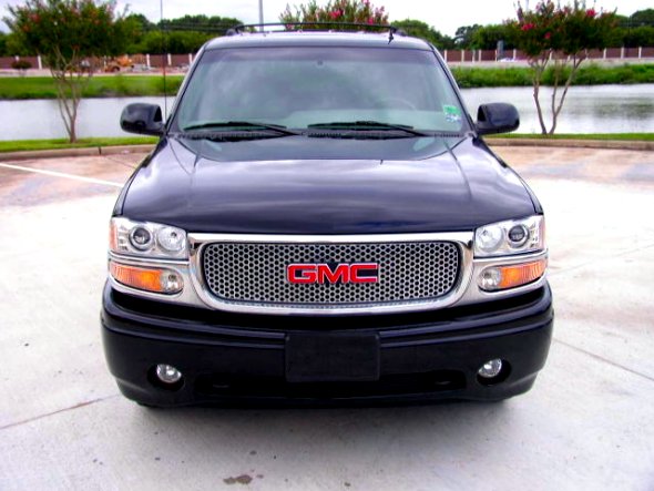 Front view of a black GMC SUV with chrome mesh grille parked on concrete near a pond