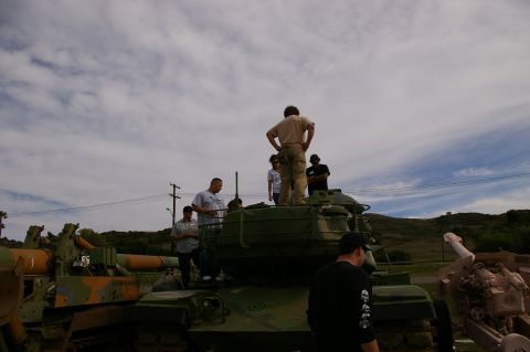 1986 Ford Bronco - Several individuals are gathered around and on top of military vehicles, including tanks and artillery, outdoors.