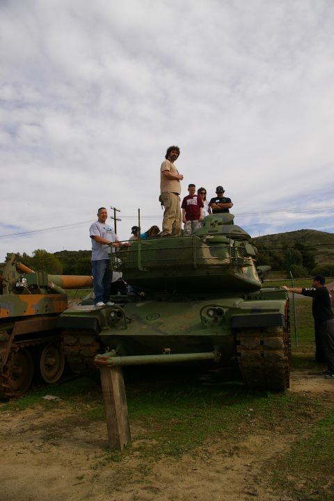 1986 Ford Bronco - Several people are gathered around and on top of military tanks in an outdoor setting.