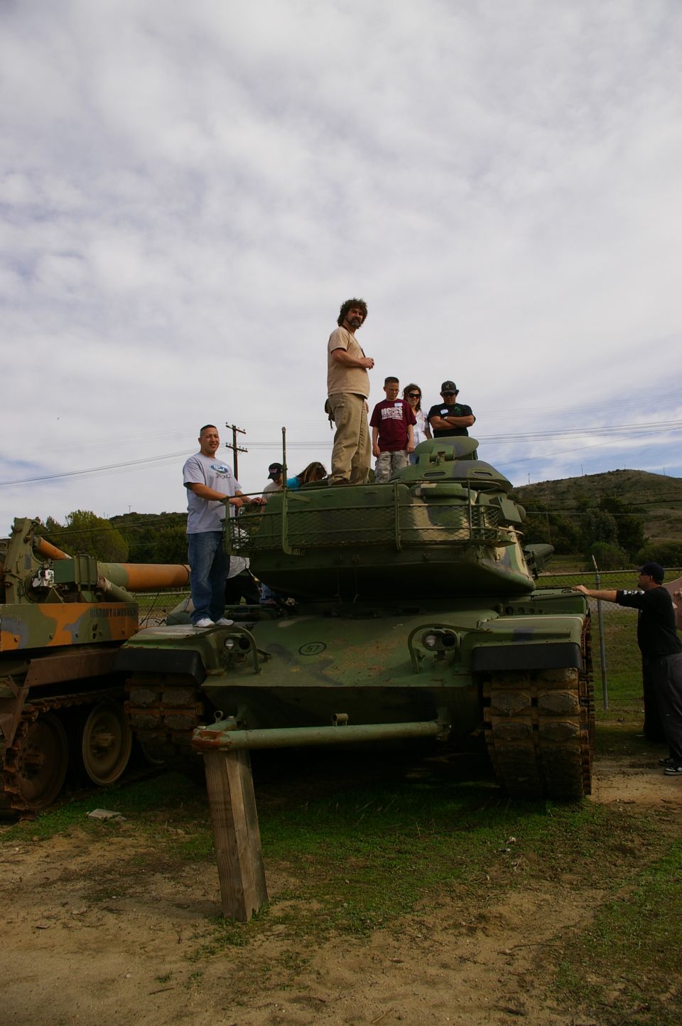 Green tanks with people standing on them under a cloudy sky
