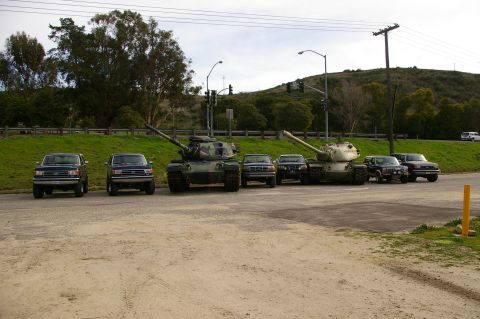 1986 Ford Bronco - Several vehicles, including two tanks and four SUVs, are parked in a line on a dirt lot.