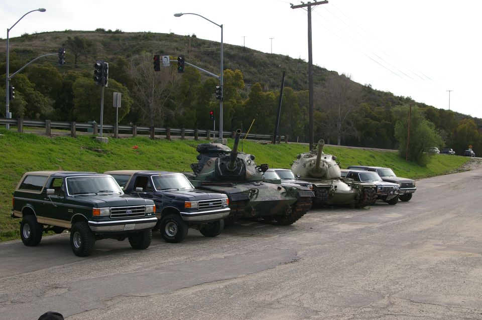 Dark green Ford Bronco and a dark blue pickup truck parked next to two military tanks on a road