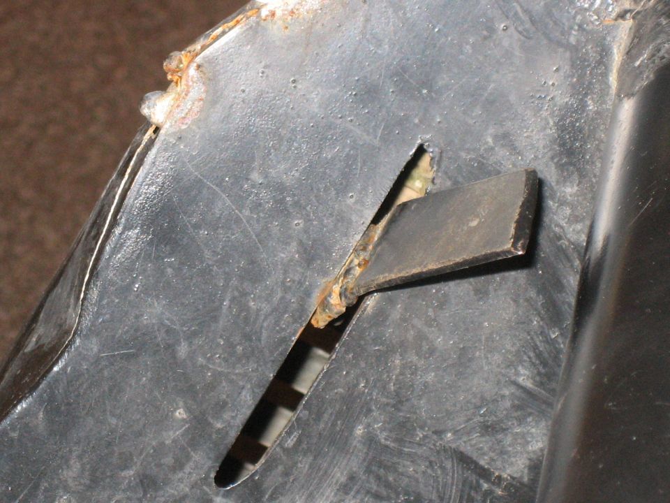close-up of a rusted metal piece with a rectangular slot cut into it, showing some wear and tear
