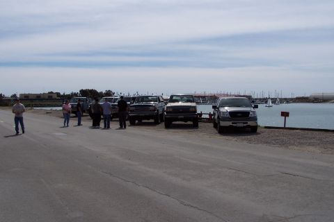 1990 Ford Bronco - Several pickup trucks are parked in a line near a marina with sailboats in the background.