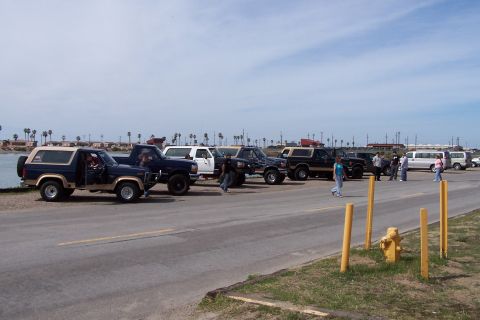 1990 Ford Bronco - A group of Ford Broncos and trucks are parked along the waterfront on a sunny day.