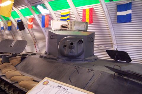 1990 Ford Bronco - A close-up view of a tank's turret and hull, with sandbags lining the exterior and signal flags visible in the background.