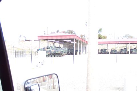 1990 Ford Bronco - Multiple military vehicles are stored under covered shelters at an outdoor facility.