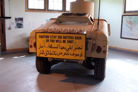 1990 Ford Bronco - A tan military vehicle is displayed with a prominent yellow warning sign in both English and Arabic.