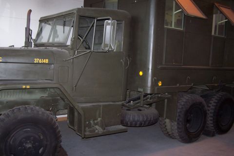 1990 Ford Bronco - A green military truck is shown from a three-quarter front view, revealing its dual rear wheels and a spare tire mounted underneath.