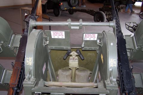 1990 Ford Bronco - A close-up view of a dual M2 Browning machine gun mount, likely in a museum setting, with other vehicles visible in the background.