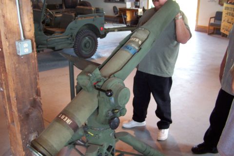 1990 Ford Bronco - A green military missile launcher is displayed indoors next to a green Jeep.
