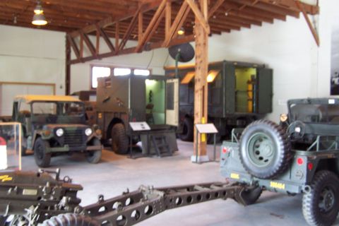 1990 Ford Bronco - A collection of military vehicles, including trucks and a jeep, are displayed indoors.