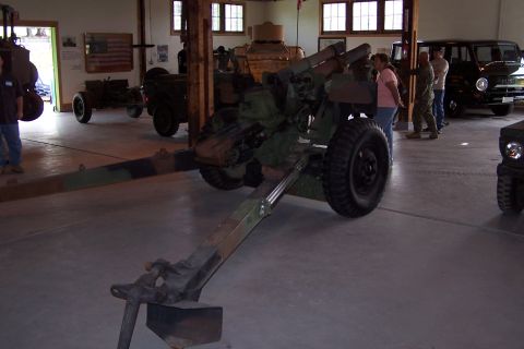 1990 Ford Bronco - An artillery piece is displayed indoors alongside other military vehicles and a tank.