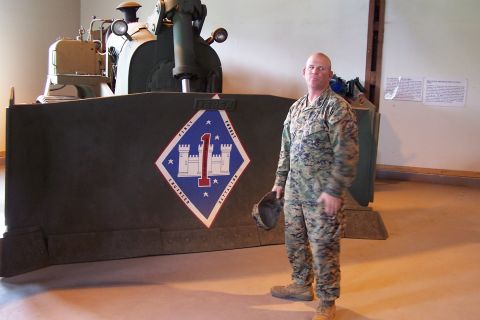 1990 Ford Bronco - A Marine poses with a large military bulldozer that has a unit emblem on its front blade.