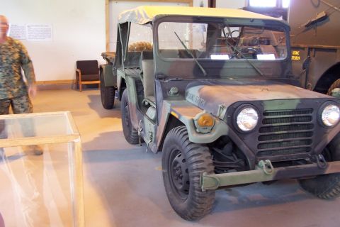 1990 Ford Bronco - A camouflaged military jeep is parked indoors, with another vehicle visible behind it and a person in uniform to the left.