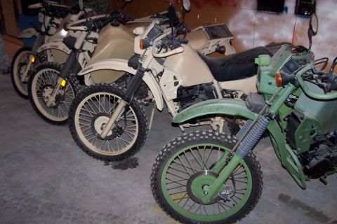 1990 Ford Bronco - Several military motorcycles are lined up in a garage, some tan and some green, with visible USMC markings on one.