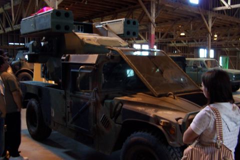 1990 Ford Bronco - Military vehicle equipped with a missile launcher is displayed indoors, with other vehicles in the background.