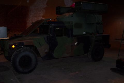 1990 Ford Bronco - This military truck, equipped with a weapon system, is parked inside a building with its hood up.