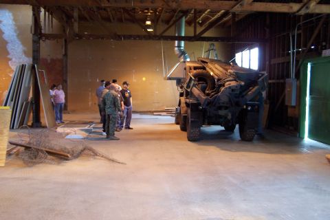 1990 Ford Bronco - A group of people observe a military truck inside a large industrial building.