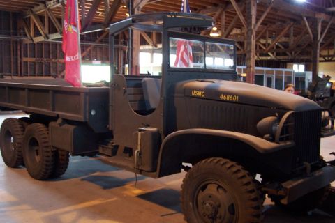 1990 Ford Bronco - A military dump truck with USMC markings is parked indoors, possibly in a museum.