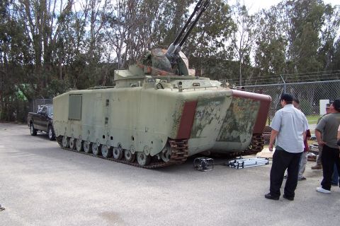 1990 Ford Bronco - Armored personnel carrier with mounted guns and a pickup truck nearby.