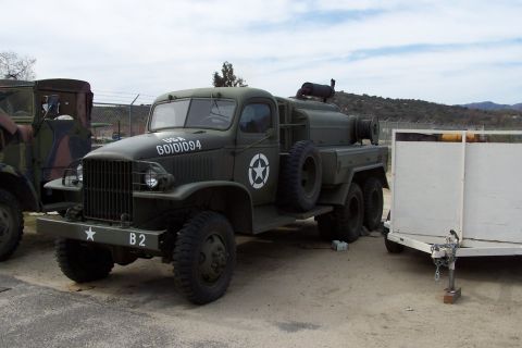 1990 Ford Bronco - A vintage military truck with a large tank on the back is parked next to a white trailer.