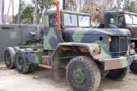 1990 Ford Bronco - This military truck, seen in a three-quarter front view, is camouflaged and features dual rear wheels and prominent exhaust stacks.
