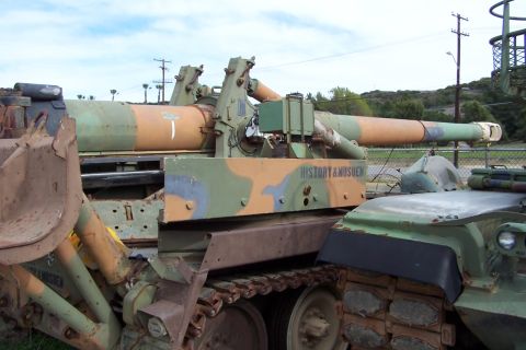 1990 Ford Bronco - A military vehicle with camouflage paint and a large cannon barrel is visible, with text reading 'HISTORY & MUSEUM' on its side.