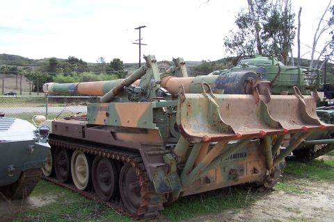1990 Ford Bronco - Military tracked vehicle with camouflage paint and a large gun barrel is parked outdoors.