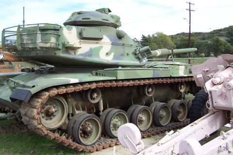 1990 Ford Bronco - A military tank with a camouflage paint scheme sits outdoors next to other equipment.