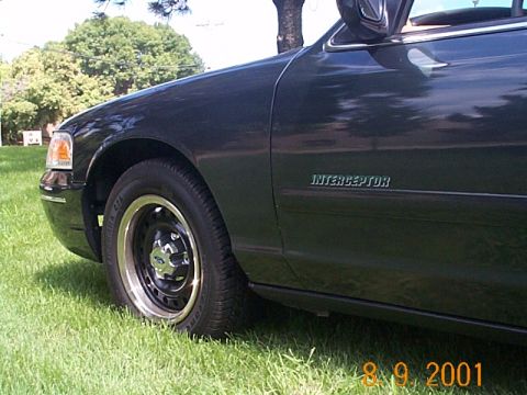 1998 Ford Crown Victoria - A dark 1998 Ford Crown Victoria Interceptor is shown from the front quarter angle, parked on a grassy area.