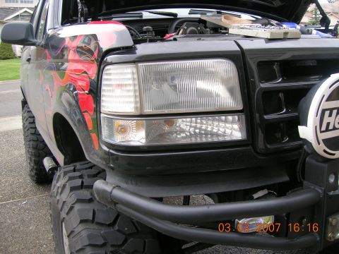 1996 Ford Bronco - This Ford Bronco has custom flame graphics and is equipped with off-road tires and a bull bar. The hood is open, revealing the engine compa…