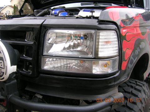 1996 Ford Bronco - Front view of a black Ford Bronco with flame decals and an open hood, revealing engine parts.