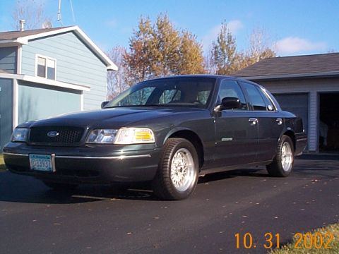 1998 Ford Crown Victoria - A dark green 1998 Ford Crown Victoria sedan is parked in front of a garage.