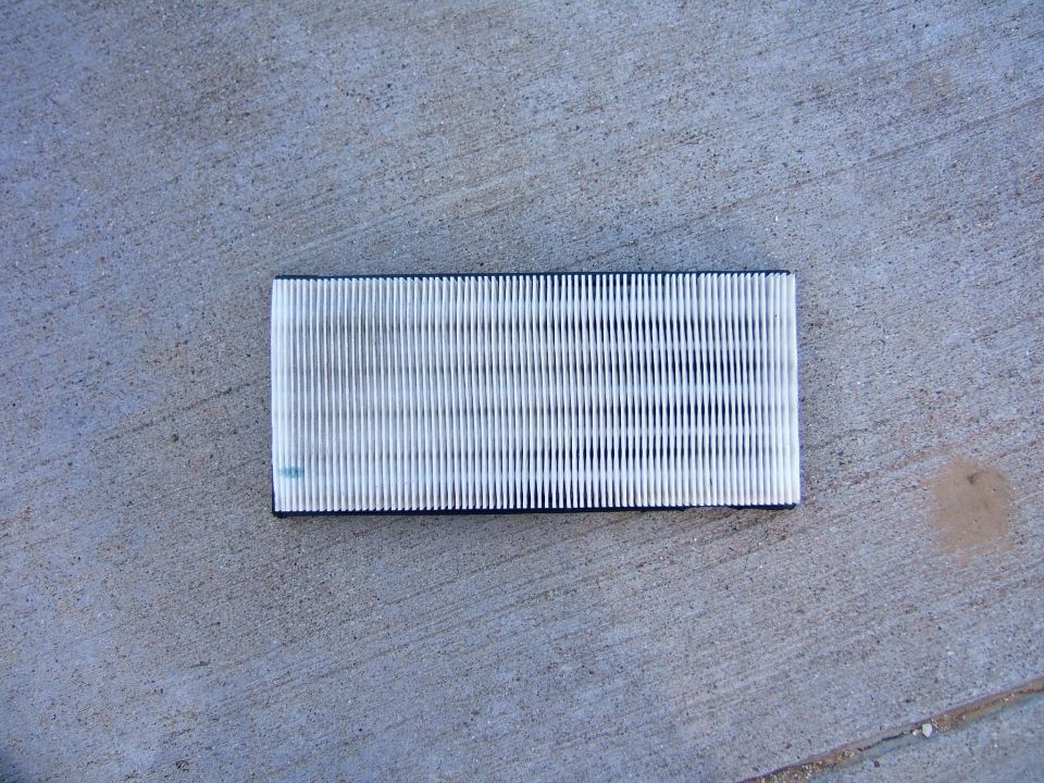White pleated panel air filter with black frame lying on concrete